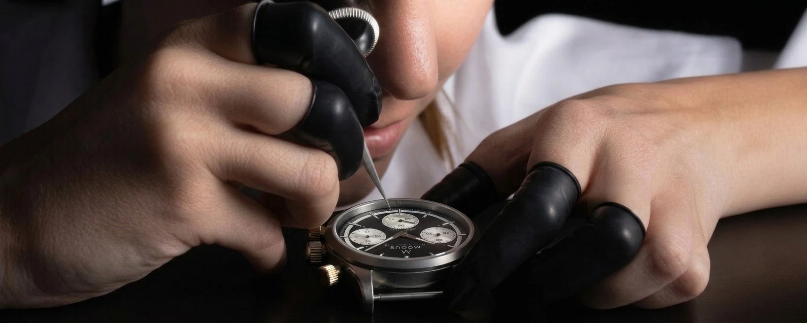 Uhrmacherin setzt mit der Pinzette einen Zeiger auf das Zifferblatt eines Modus-Chronographen