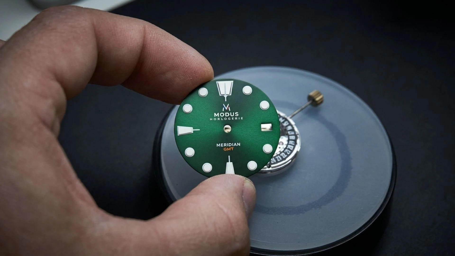 Hand hält ein grünes Modus-Zifferblatt über einem Uhrwerk, vor dem Einbau in eine Uhr